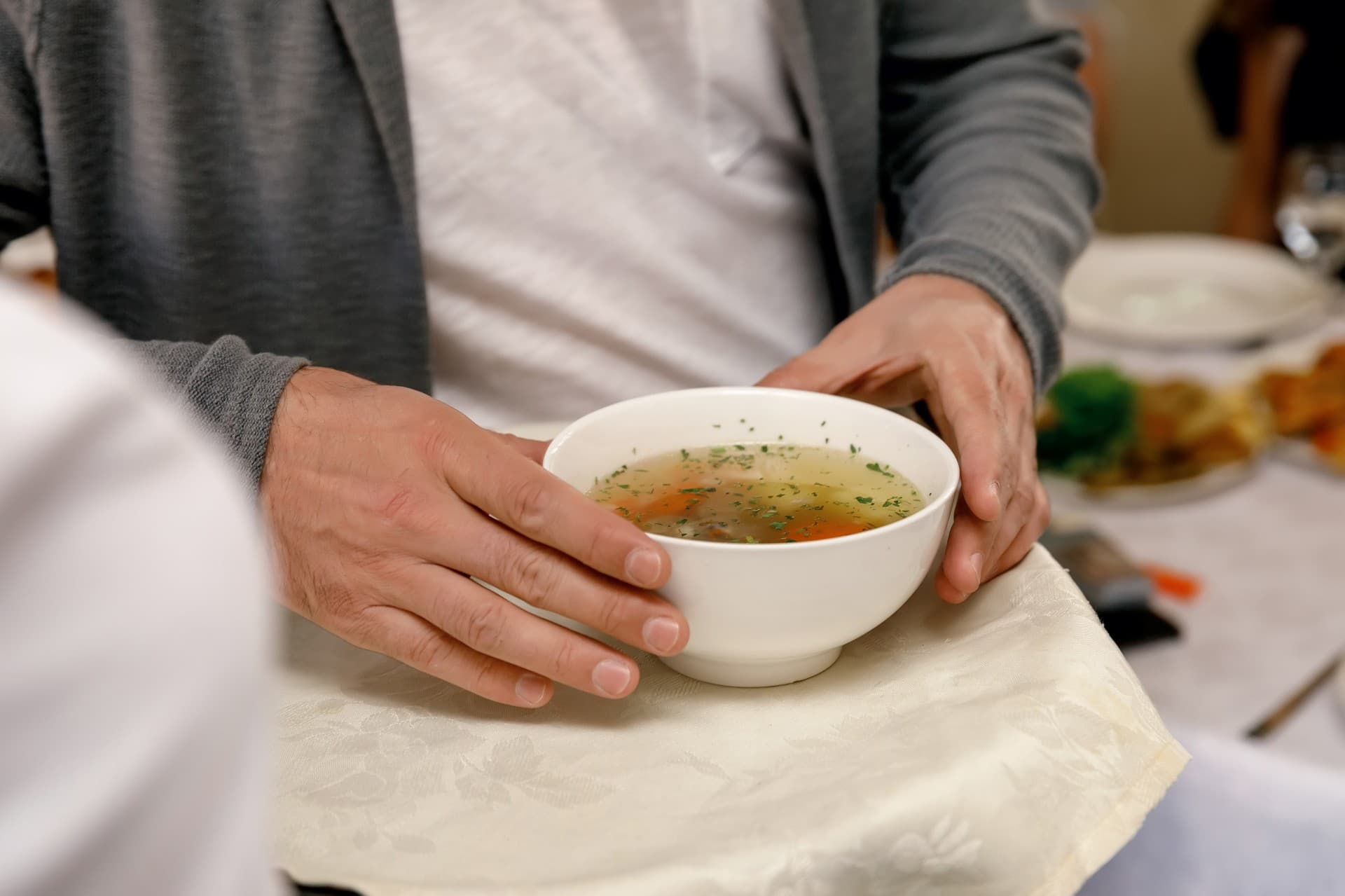 adult man holding white bowl chicken soup his hands